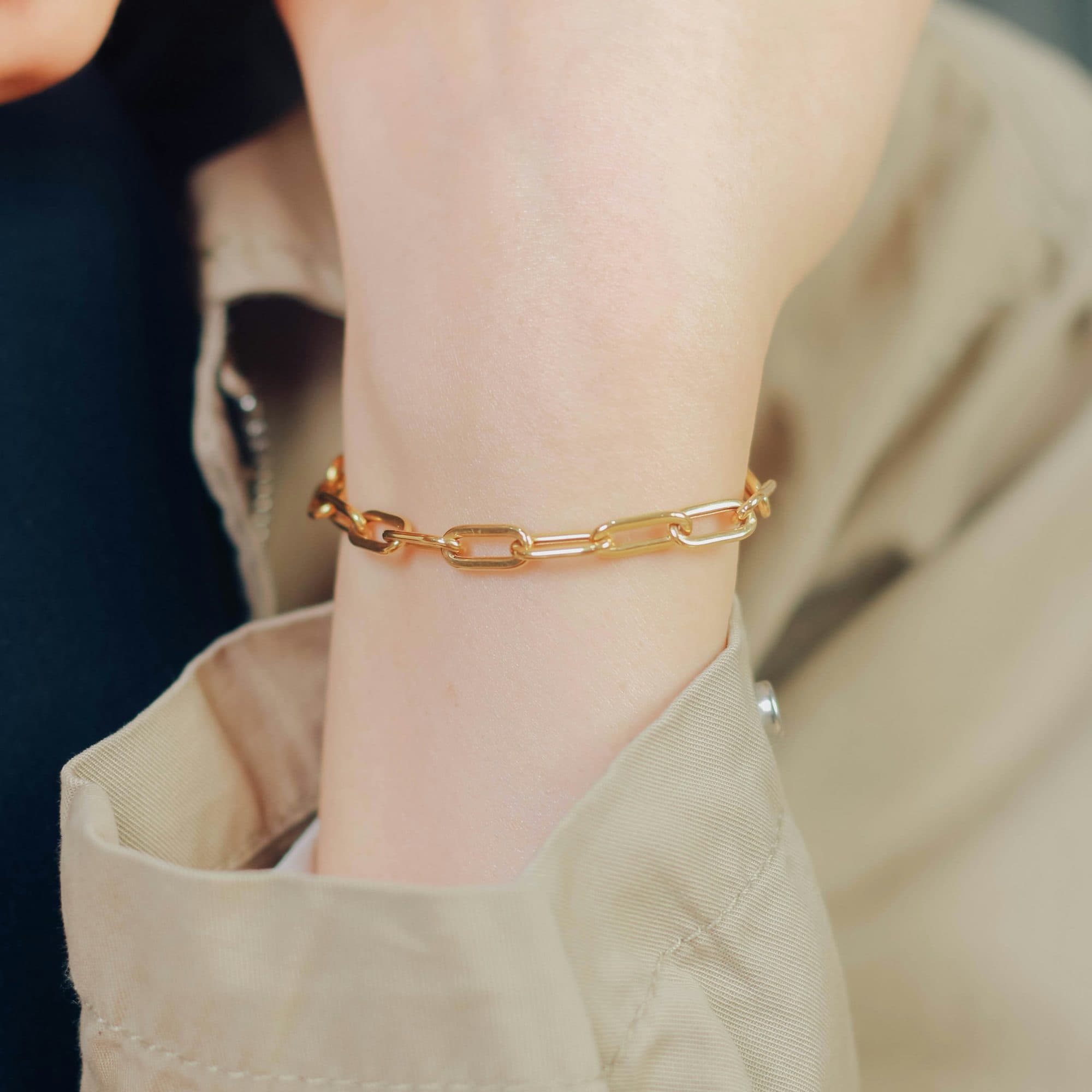 Pulseira de elos em ouro usada no dia a dia, sobre o punho de um trench