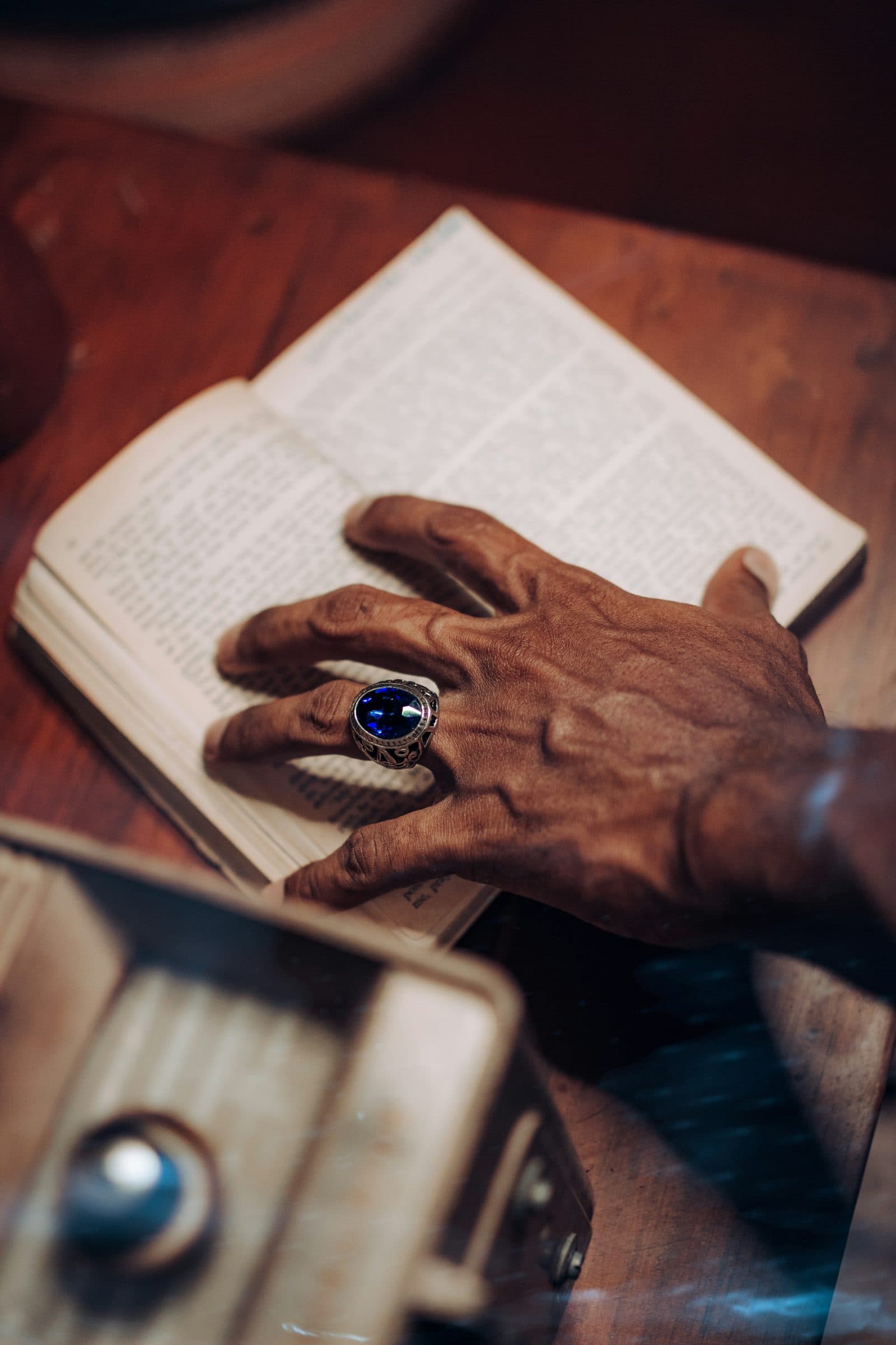 Mão madura com um anel de pedra azul, pousada sobre um livro aberto
